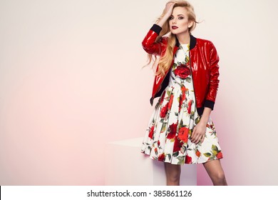 Beautiful Young Blonde Woman In Nice Spring Dress And Red Plactic Jacket Posing In A Studio. Fashion Photo