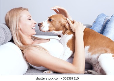 Beautiful young blonde woman playing with her dog at home, smiling. Happiness.
