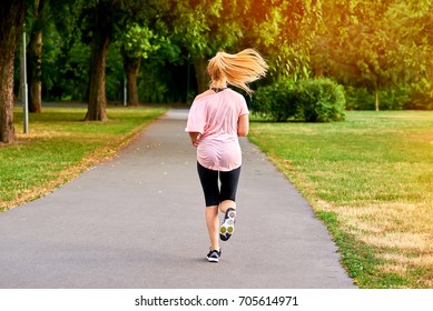 A Beautiful Young Blonde Woman Running Away From The Camera On The Road In A Park
