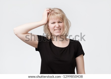 Beautiful young blonde woman scratching the head trying to remember hometask.