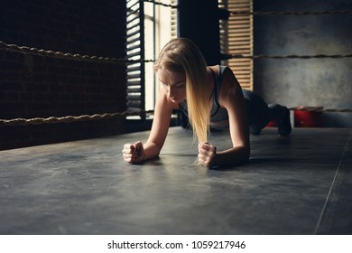 Beautiful young blonde woman in sports clothes exercising indoors, doing elbow plank inside boxing ring, testing endurance, having concentrated focused look. Athletic sporty girl training in gym - Powered by Shutterstock