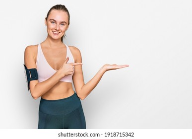 Beautiful young blonde woman wearing sportswear and arm band amazed and smiling to the camera while presenting with hand and pointing with finger.  - Shutterstock ID 1918715342