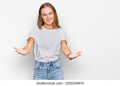 Beautiful young blonde woman wearing casual white t shirt smiling cheerful offering hands giving assistance and acceptance. 