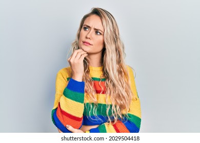 Beautiful young blonde woman wearing colored sweater with hand on chin thinking about question, pensive expression. smiling with thoughtful face. doubt concept. 