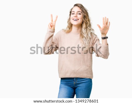 Beautiful young blonde woman wearing sweatershirt over isolated background showing and pointing up with fingers number seven while smiling confident and happy.