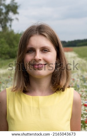 a beautiful young blonde woman in a yellow dress stands among a flowering field