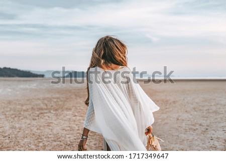 beautiful young boho woman walking on the beach at sunset