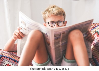 Beautiful Young Boy Reading A Newspaper At Home. Blonde Child Reads News On A Journal. Generation Z Child Looking Last-minute News On A Paper Magazine. Information Interest Culture Educational Concept