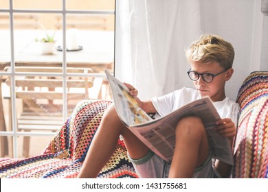 Beautiful Young Boy Reading A Newspaper At Home. Blonde Child Reads News On A Journal. Generation Z Child Looking Last-minute News On A Paper Magazine. Information Interest Culture Educational Concept