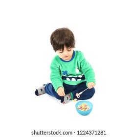 Beautiful Young Boy Sitting Down Next To A Bowl Of Cereals Against A White Background