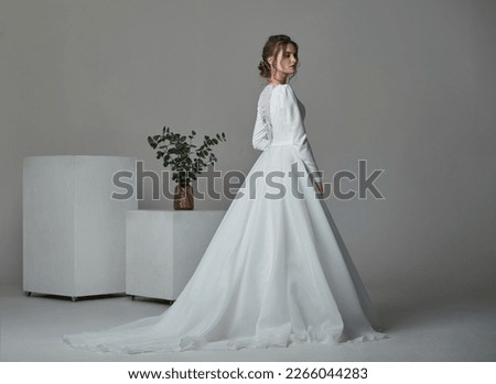 A beautiful young bride model in long lace dress in minimalist white studio interior. Wedding photography.