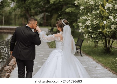 Una bella joven novia camina con su novio en el parque de verano. Foto de la novia y el novio desde atrás. Hermoso vestido blanco de boda. Camina por el parque. Una pareja feliz y amorosa.