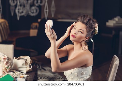 Beautiful Young Bride Wearing Fashion Gown Sitting On Chair And Looking Into Hand Mirror