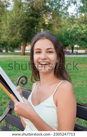 Beautiful young brownhair girl is reading the book and enjoys the smell of a fresh printed book sitting on the bench in the park. Stock photo © 