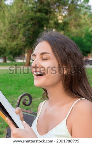 Beautiful young brownhair girl smells a fresh printed book sitting on the bench in the park. Stock photo © 