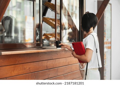 A Beautiful Young Brunette Business Woman With A Short Bob Haircut Is Standing Near An Outlet With Coffee And Ready-made Food And Waiting For Her Order