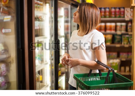 Beautiful young brunette doing some shopping at a supermarket and looking at a refrigerator