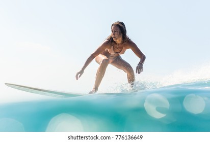 Beautiful young brunette girl in a bikini swimsuit ride big wave. Sporty surfer woman surfing in Mauritius in the Indian Ocean on the background of blue sky, clouds and transparent waves. Hippie life.