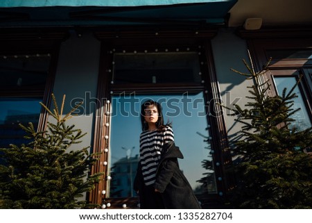 beautiful young brunette girl in black coat walking along city street, woman is relaxing outdoors