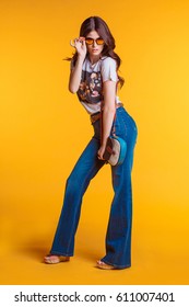 Beautiful young brunette girl wearing white t-shirt jeans flared with a small bag standing on a yellow background in the Studio. - Shutterstock ID 611007401