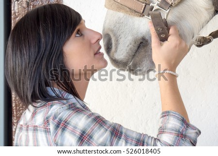 Beautiful young brunette girl and white horse in the stable