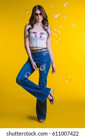 Beautiful young brunette with glasses in white top and jeans flared standing on a yellow background in the Studio in full growth.Fashion looks elegance clothes..bubbles - Shutterstock ID 611007422