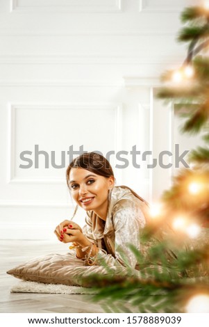 Beautiful young brunette in golden Christmas fashionable sweat suit.Christmas tree and presents.Interior of luxury apartment with ecological fireplace.Decorating candles and Christmas lights.Copy spac