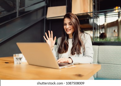 Beautiful young brunette is having Skype call on her laptop while sitting in cafe - Shutterstock ID 1087508009