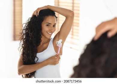 Beautiful Young Brunette Lady Shawing Armpit With Razor In Bathroom, Smiling Millennial Woman Using Shave Cream While Making Underarm Hair Depilation Near Mirror At Home, Closeup With Selective Focus