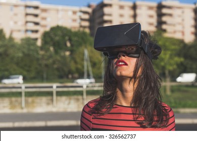 Beautiful young brunette with long hair wearing virtual reality headset in an urban context