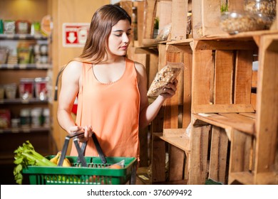 Beautiful Young Brunette Looking At A Product Label While Buying Some Groceries At The Super Market