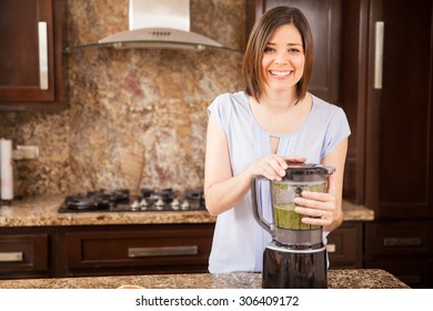 Beautiful Young Brunette Making Some Green Juice In A Blender At Home And Smiling