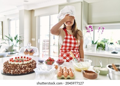 Beautiful Young Brunette Pastry Chef Woman Cooking Pastries At The Kitchen Smiling And Laughing With Hand On Face Covering Eyes For Surprise. Blind Concept. 