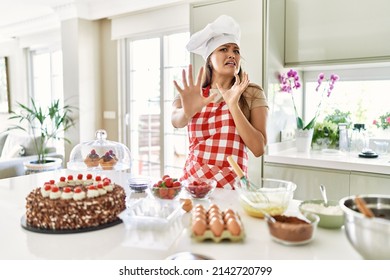 Beautiful young brunette pastry chef woman cooking pastries at the kitchen afraid and terrified with fear expression stop gesture with hands, shouting in shock. panic concept. 