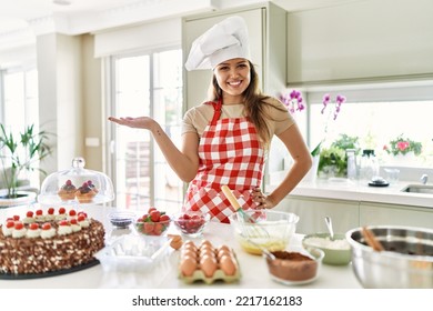 Beautiful young brunette pastry chef woman cooking pastries at the kitchen smiling cheerful presenting and pointing with palm of hand looking at the camera.  - Powered by Shutterstock