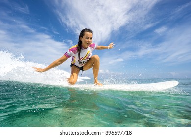Beautiful young brunette woman in a bright bikini surfing in Mauritius in the Indian Ocean on the background of blue sky, clouds and transparent waves