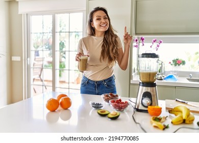 Beautiful young brunette woman drinking glass of smoothie at the kitchen surprised with an idea or question pointing finger with happy face, number one  - Shutterstock ID 2194770085