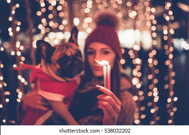 Beautiful young brunette woman with French bulldog enjoying Christmas or New Year night on a city street. Selective focus on woman's hand.