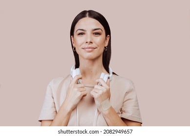 Beautiful young brunette woman girl in beige shirt posing isolated on beige wall background studio portait. Listening music with headphones. People lifestyle concept. Mock up copy space.