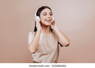 Beautiful Young Brunette Woman Girl In Beige Shirt Posing Isolated On Beige Wall Background Studio Portait. Listening Music With Headphones. People Lifestyle Concept. Mock Up Copy Space.