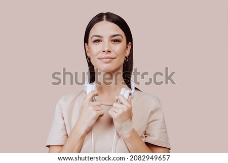 Beautiful young brunette woman girl in beige shirt posing isolated on beige wall background studio portait. Listening music with headphones. People lifestyle concept. Mock up copy space.
