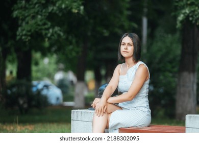 Beautiful Young Brunette Woman With A Short Bob Haircut Sits On A Bench In The City Park For A Walk