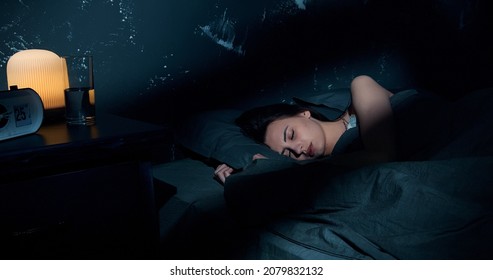 Beautiful young brunette woman sleeping on side, lying cozily in bed, hugging a pillow. Lady sound asleep at night. Loft interior.