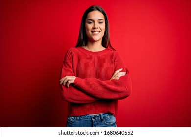 Beautiful young brunette woman wearing casual sweater standing over red isolated background smiling with happy face winking at the camera doing victory sign. Number two.