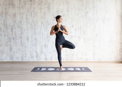 Beautiful Young Brunette Woman Yoga Instructor Doing Vrikshasana On A Mat In A Wooden Floor Standing In The Gym With Day Lighting