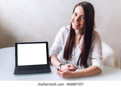 A beautiful young business lady makes a presentation sitting and smiling in front of a white table, uses a tablet with mockup screen - Shutterstock ID 406887337