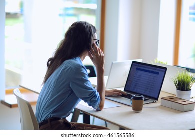 Beautiful Young Business Woman Sitting At Office Desk And Talking On Cell Phone