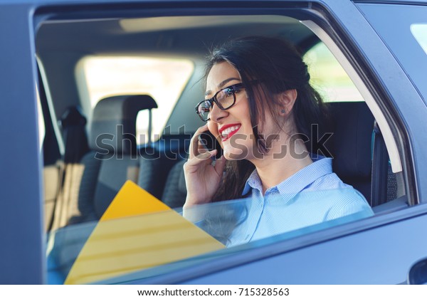 Beautiful young business woman sitting\
in the car looking at her planner and talking at\
phone.