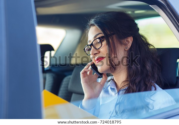 Beautiful young business woman sitting\
in the car looking at her planner and talking at\
phone.