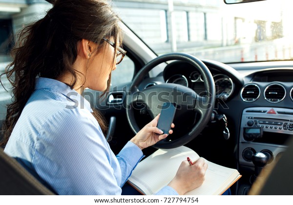 Beautiful young business woman sitting in the\
car looking at her\
planner.
